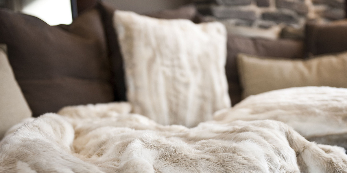 Kuschelige weiße Decke mit Kissen auf einem Sofa.